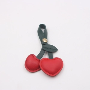 Detail shot of the red leather cherry charm with green leaves and gold metal snap hook