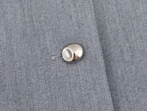 Macro view of grey crepe fabric texture and silver metallic button on a two-piece dress