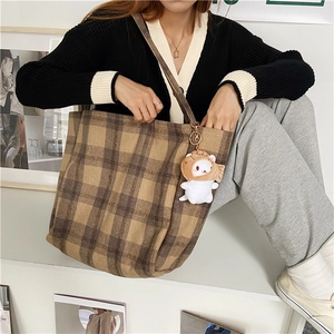 Macro detail of large plaid tote bag featuring a cute cat plush charm in home setting