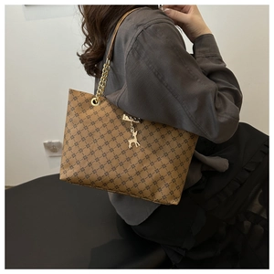 Detail of brown tote bag featuring geometric monogram print and gold deer pendant charm