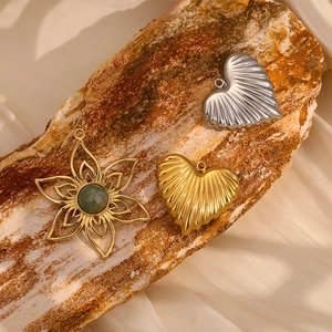 Close-up of gold flower pendant with green gemstone and heart charms on rustic wood