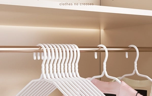 Close-up of white non-slip plastic hangers hanging neatly in a wooden wardrobe cabinet