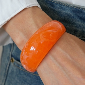 Close-up of vibrant orange marble resin wide cuff bracelet styled with denim