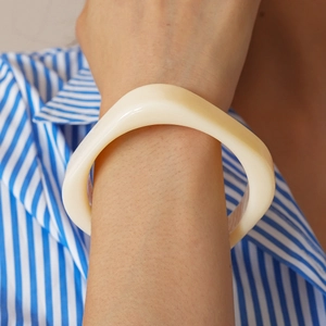Close-up of a wavy thick resin bangle in cream color worn with a striped shirt