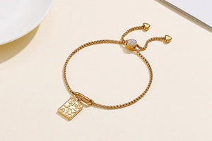 Detail of gold square link bracelet with lucky symbols charms and adjustable slider clasp