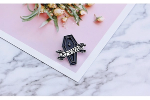Detail of coffin-shaped enamel brooch featuring Let's Hide ribbon on marble background