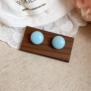 Close-up of light blue round enamel stud earrings on a vintage dark walnut wooden stand