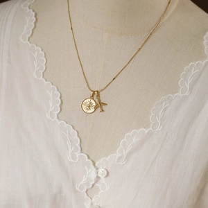 Close-up of gold titanium steel necklace featuring sun god compass and airplane pendants