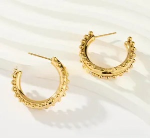 Detail of high-polished gold C-shape hoop earrings with decorative beaded edges on a white stand