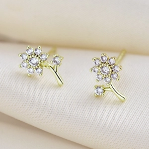 Detalle macro de pendientes de margarita dorados con circonitas sobre seda beige suave