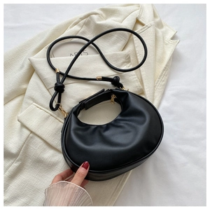 Close-up of minimalist black crescent bag with golden zipper and leather knot detail