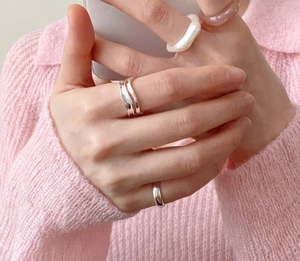 Close-up of minimalist wave-shaped 925 silver rings on a hand with pink knitwear background