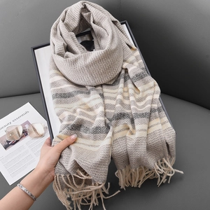 Striped warm winter scarf with tassels and herringbone pattern on a stylish grey sofa