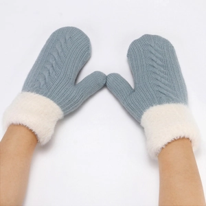 Detailed close-up of blue knitted cable mittens with white plush cuffs worn by a model