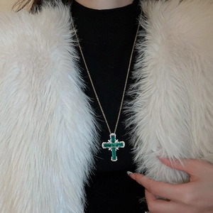 Détail d'un collier pendentif croix en zircon vert porté sur un manteau de fourrure blanc