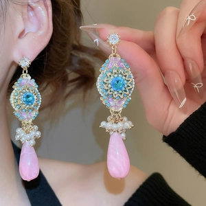 Close-up of bohemian gold earrings with blue stones and pink teardrop pendants on model