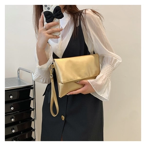 Detalle de bolso sobre color oro champán con acabado metálico liso y correa de muñeca