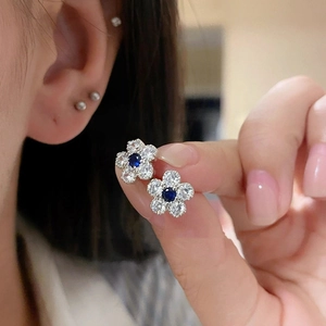Detailed macro shot of a silver flower stud earring with a blue central zircon stone