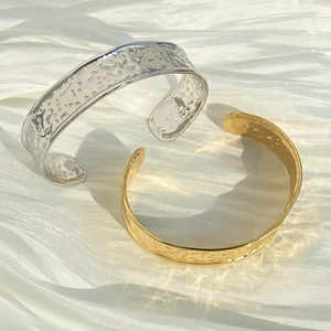 Textured irregular wide cuff bangles in gold and silver finish on white satin fabric