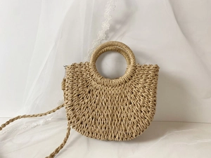 Detail of a semi-circular straw bag with woven handles and strap on white lace