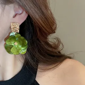 Boucles d'oreilles fleur élégantes avec pétales en acrylique vert et clous dorés sur modèle