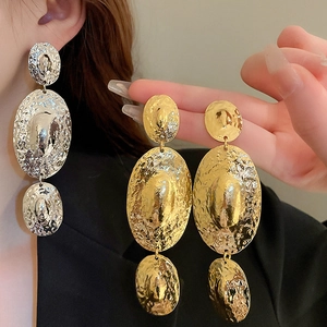 Detail of long drop metal earrings with hammered texture in gold and silver finish
