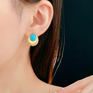 Detail of vintage gold fan-shaped earring with turquoise stone worn by model