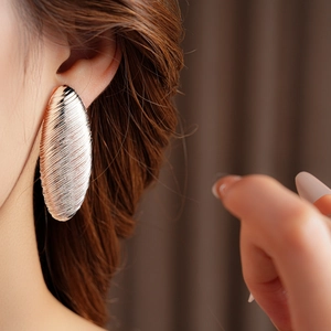 Close-up of golden oval textured hoop earring with brushed finish on a model's ear