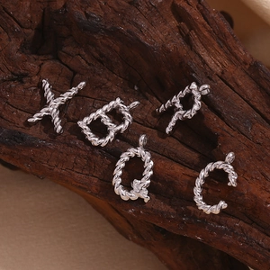 Macro detail of silver twisted rope letter pendants X, D, P, Q, C on wooden background