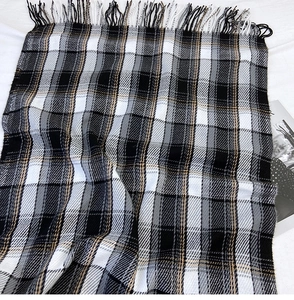 Detailed view of British plaid scarf with grey black white checks and long tassel edges