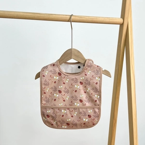Waterproof baby bib with brown floral print and food catcher pocket on a wooden hanger