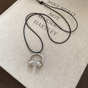 Detailed view of silver headphone pendant necklace on a book for a stylish look