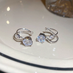Detail of silver double-layered ear cuff with round zircons on a white ceramic plate