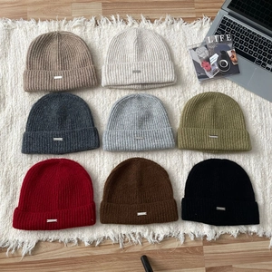 Flat lay of knit beanies in multiple colors including beige, grey and olive green