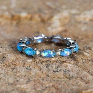 Macro shot of eternity ring with blue oval opals and white zircons on rock surface