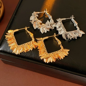 Close-up of gold and silver leaf square hoop earrings on a black leather jewelry box