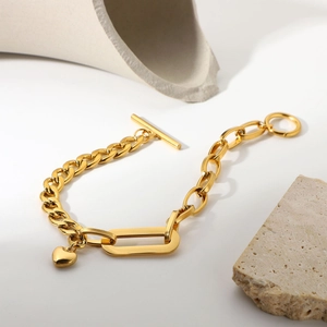 Macro detail of golden Cuban chain bracelet with heart pendant and OT toggle clasp