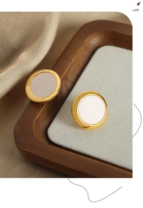 Detail of round gold-plated earrings with cream enamel inlay on a grey velvet display pad