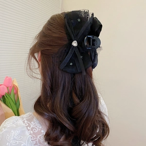 Détail d'une pince à cheveux en dentelle noire avec strass en cœur sur cheveux ondulés