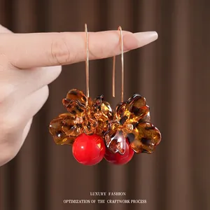 Floral leopard print drop earrings with amber petals and red beads held by hand