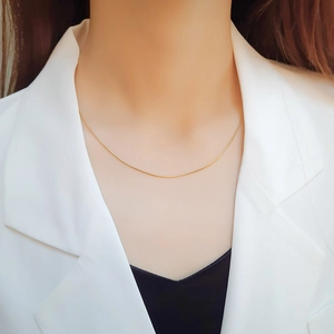 Close-up of minimalist 1mm gold snake bone chain worn by model in elegant business attire