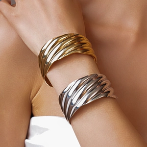 Detailed view of wide metallic cuff bracelets with wavy texture in gold and silver finish