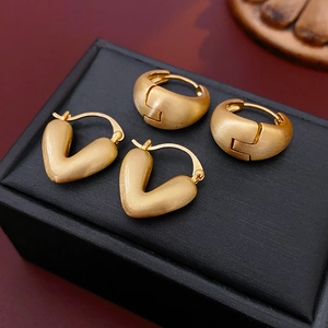 Macro view of matte gold brushed geometric heart and hoop earrings on black leather display