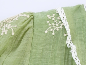 Close-up of green pleated fabric with white floral embroidery and delicate lace details