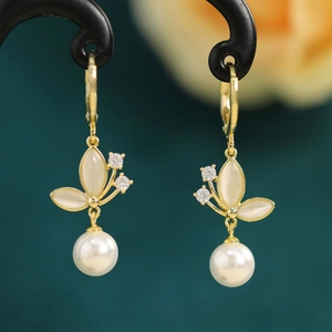 Close-up of golden butterfly earrings with opal stone and hanging round white pearl