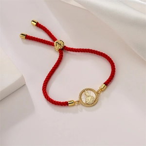 Close-up of red woven adjustable bracelet with golden religious medal on silk