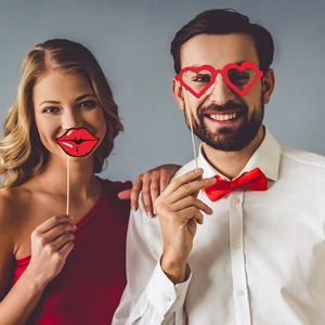 Close-up of couple using red heart glasses and lips paper photo props for Valentine party