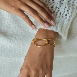 Detail of gold double-ring interlocking chain bracelet on a model with white knitwear