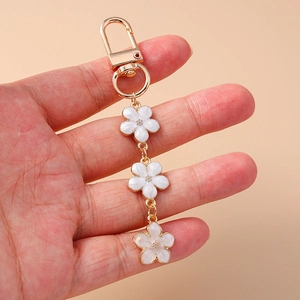 Detail of white enamel sakura flower pendants on a gold keychain held in hand