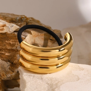 Close-up of triple-layered gold metal hair ring with black elastic hair tie on stone